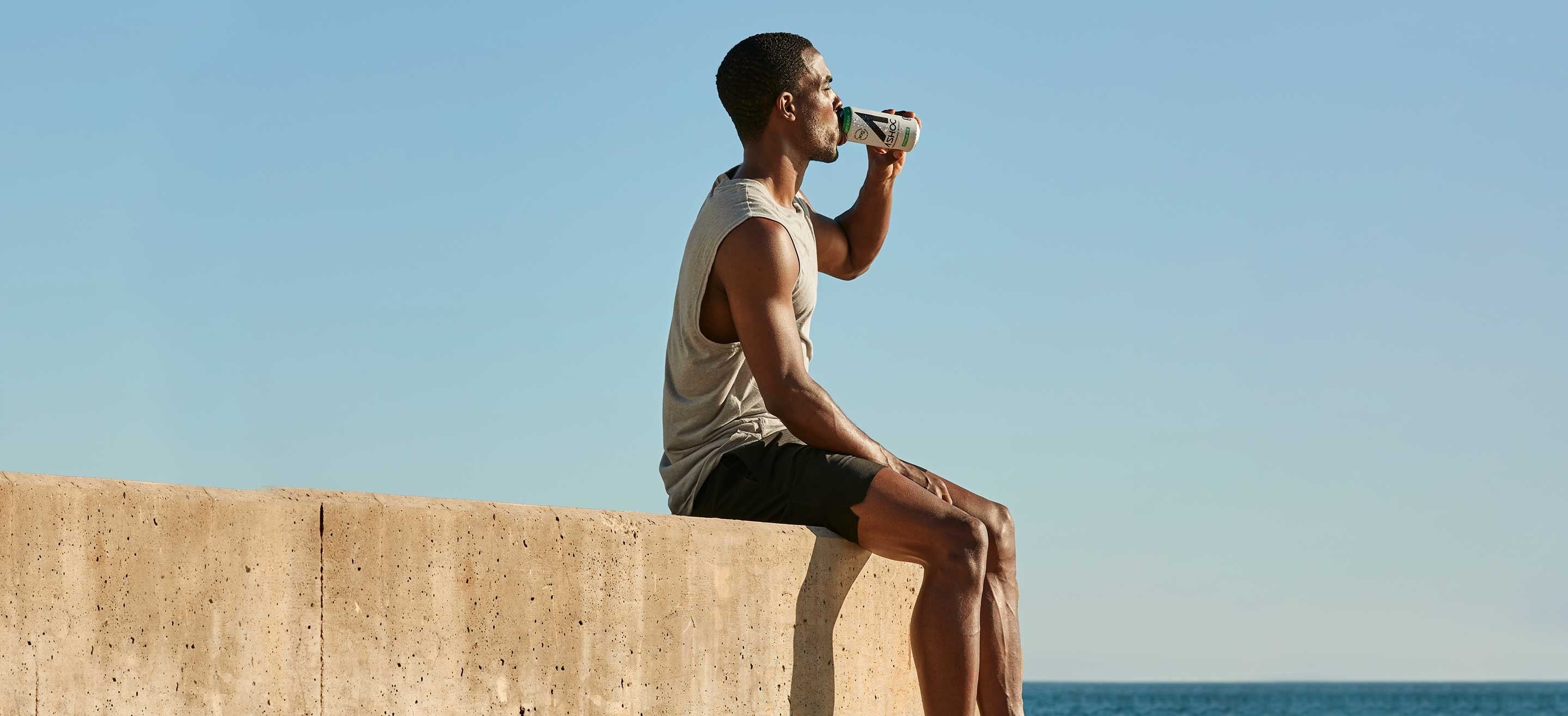 Man sitting on wall overlooking the ocean drinking Ashoc.