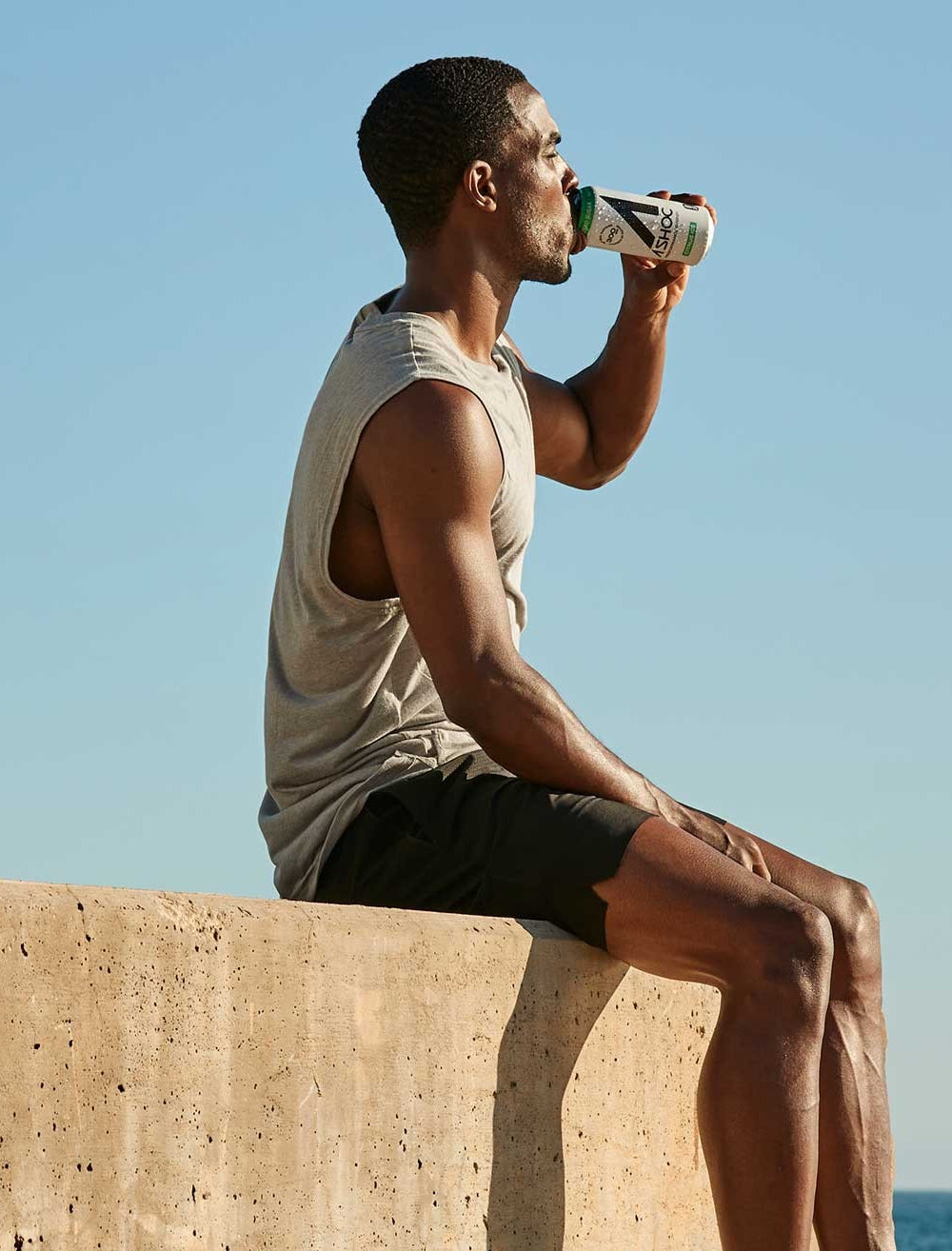 Man sitting on wall overlooking the ocean drinking Ashoc.